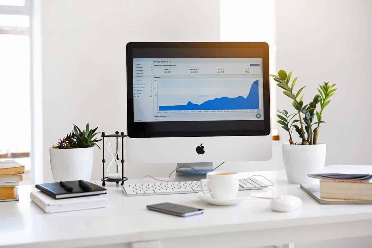 Postazione di lavoro moderna con iMac che mostra grafici di crescita SEO, circondato da piante, taccuini e tazza di caffè su una scrivania bianca