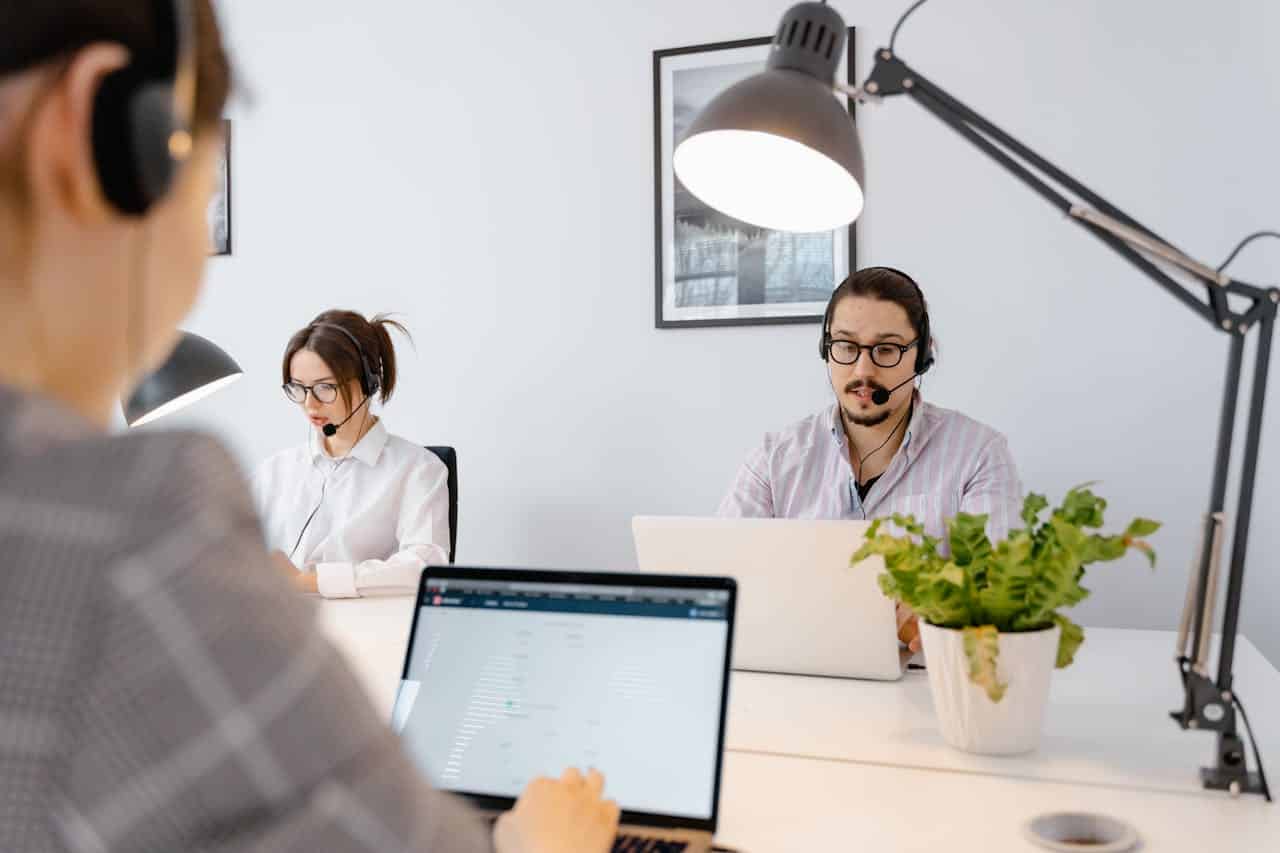 Operatori di call center outbound al lavoro con cuffie e laptop in un ufficio moderno e luminoso.