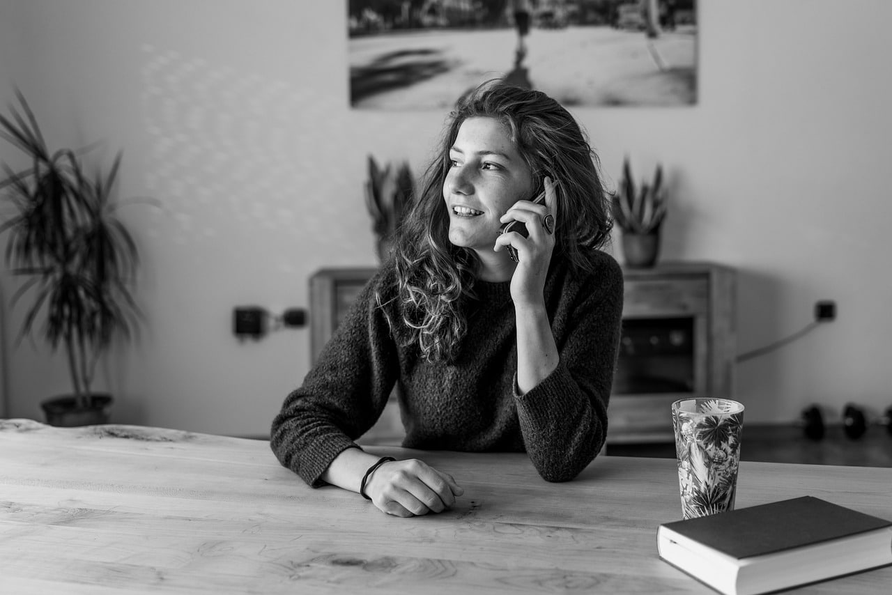 Donna sorridente al telefono seduta a un tavolo,